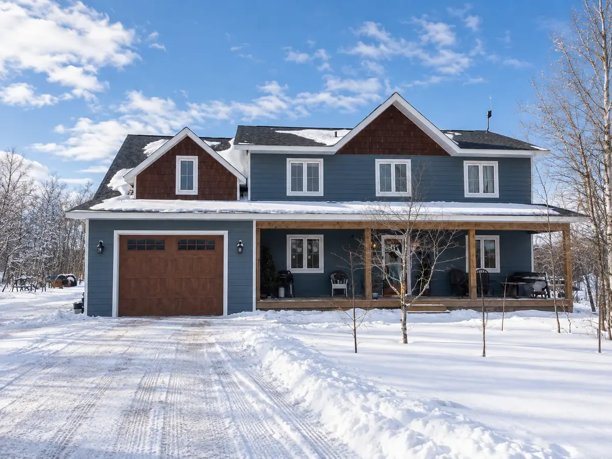 Two-storey house in Giroux with blue LP siding, cedar shake gables and a covered front porch, in winter